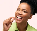 Person smiling and holding a pink pill between fingers.