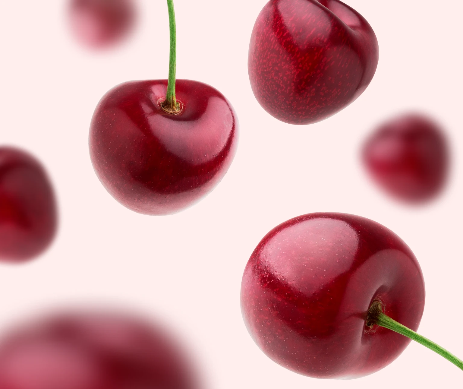 Red cherries with stems arranged on a light pink background.