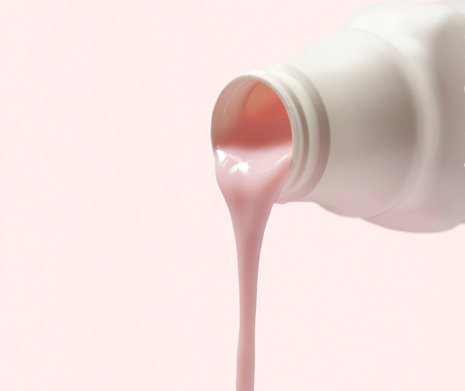 Pink liquid pouring from a white bottle against a light pink background.