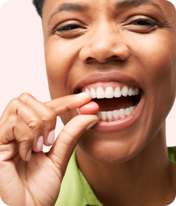 Woman smiling while holding a pill near her mouth.