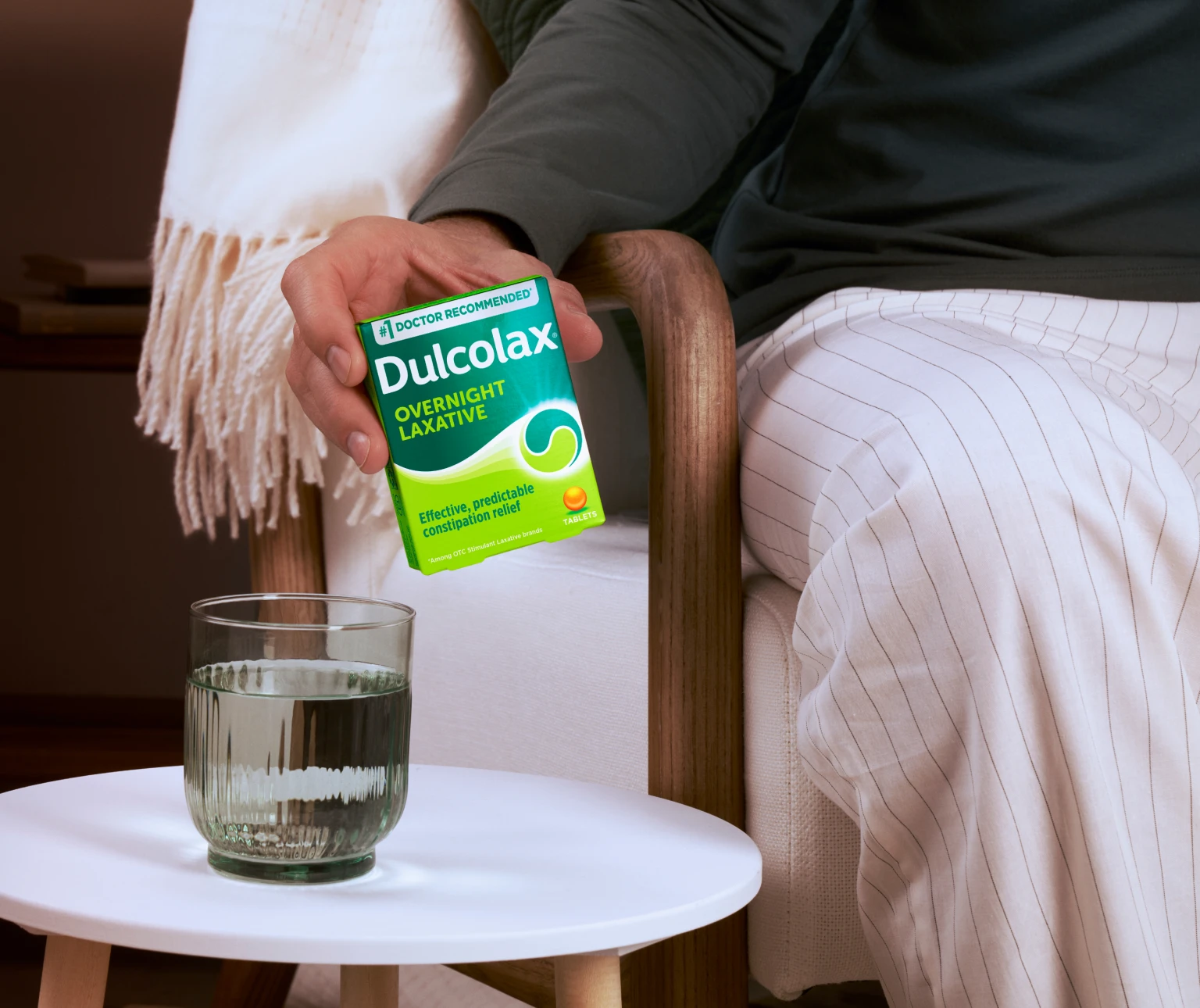 A person holds a box of Dulcolax Overnight Laxative tablets next to a glass of water on a table.
